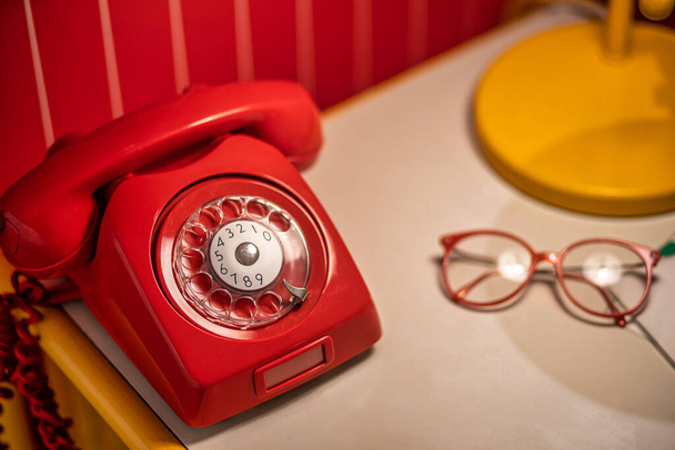 Imagen de Teléfono rojo antiguo con esfera giratoria sobre la mesa con cristales viejos
 - Foto, imagen