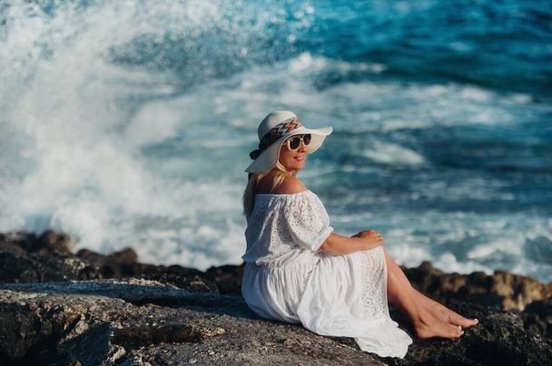 Girl sitting on the shore of the Atlantic Ocean in a white dress and a straw hat - Фото, зображення