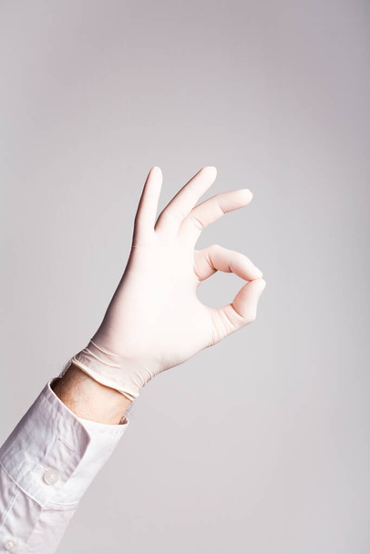 Male hand in a medical glove shows OK on a white background - 写真・画像
