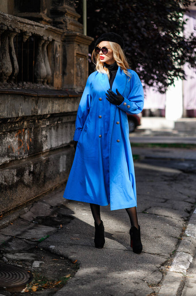 Fashionable model in a blue cloak posing near old wall - Valokuva, kuva