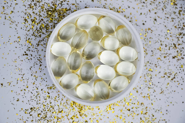 Витамин D3 желатиновые капсулы на белом фоне. Жирорастворимый солнечный витамин холекальциферол светится желтым и блестит. Место для текста
 - Фото, изображение