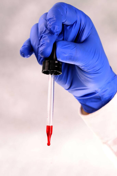 Vertical view of a medical worker's hand with protective glove, holding a pipette with blood sample, on a white background. Coronavirus test. A corona . - Foto, Bild