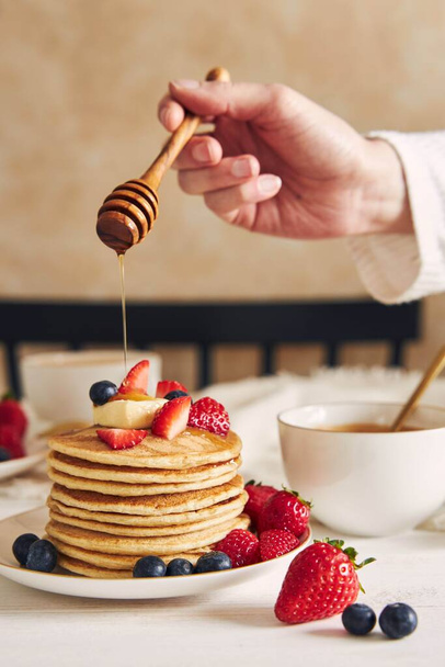 A vertical shot of a person putting syrup on vegan tofu pancakes with fruits - 写真・画像