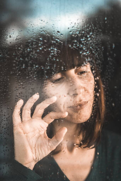 Un disparo vertical de una mujer mirando por la ventana durante la pandemia en un día lluvioso - Foto, imagen
