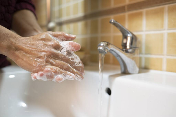 Egy közelkép egy nőről, amint szappannal mossa a kezét a fürdőszobában, felhívva a figyelmet a jelenlegi járványhelyzetre. - Fotó, kép