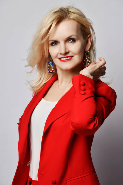 Portret van jonge mooie blonde glimlachende vrouw gelukkig glimlachen in stijlvolle elegante diep rood officieel pak en enorme oorbellen  - Foto, afbeelding