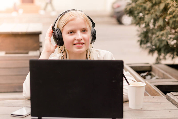 Mladá dívka sedí venku v kavárně s notebookem a velkými sluchátky - Fotografie, Obrázek