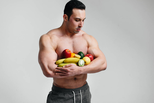 Sportlicher, sexy Typ, der auf weißem Hintergrund mit leuchtenden Früchten posiert. Ernährung. Gesunde Ernährung - Foto, Bild