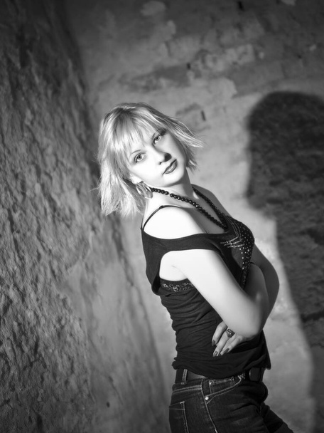 Conceptual portrait of a modern and young, seductive, emotional, beautiful blonde, girl, woman, in a dark blouse, in the interior of a destroyed building, walls, brick - Zdjęcie, obraz