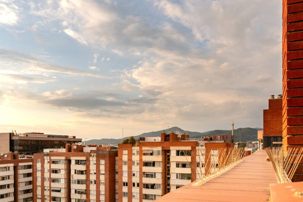 A view of buildings from a balcony surrounded by hills under the sunlight and a cloudy sky at daytime - 写真・画像