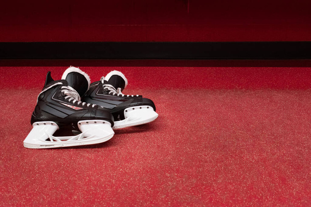 Hockey skates lying over red floor in locker room with copy space  - Fotó, kép
