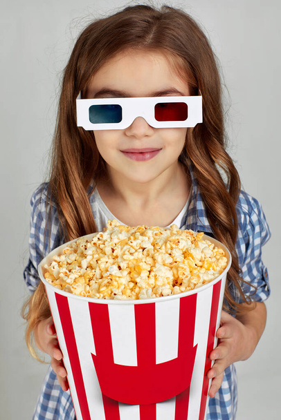 child girl in red-blue 3d glasses holding popcorn bucket - Zdjęcie, obraz