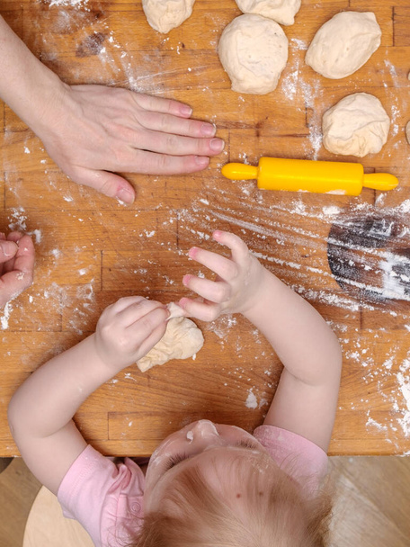 Hands of mother and little daughter knead the dough on a wooden table. Flat lay. The concept of family cooking baking bringing together parents and children. - Photo, image