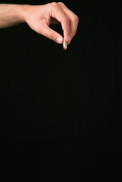 A vertical shot of a person holding a bullet with a black background - Foto, immagini