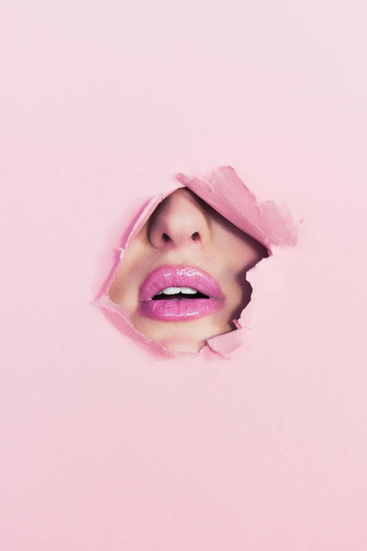 A closeup vertical shot of a female's face part under the pink torn wall - Fotó, kép