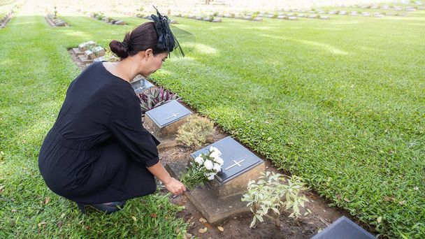 Truchlící mladá žena pokládající bílé květy na její rodinný hrob v krásné zelené hřbitově. - Fotografie, Obrázek