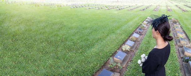 Jeune femme en deuil tenant des fleurs blanches sur sa tombe familiale dans un beau cimetière vert
. - Photo, image