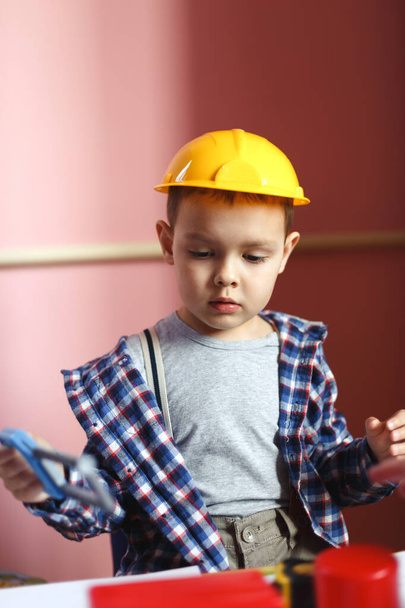 Kleiner Junge mit Helm spielt in Werkstatt mit Plastikschlauch. - Foto, Bild