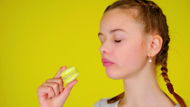 Tini lány harap egy sárga macaroon és élvezi a páratlan íze - Felvétel, videó