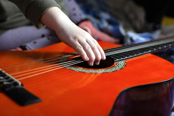 Kinderhand zieht die Saiten einer orangefarbenen Akustikgitarre - Foto, Bild