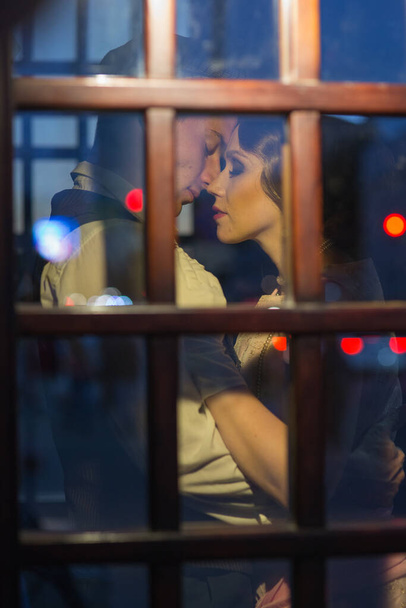 Nuori mies syleilee naistaan ja haluaa suudella häntä. Ne ovat lasiovien takana. Retropuvuissa. Historiallinen jälleenrakennus
 - Valokuva, kuva