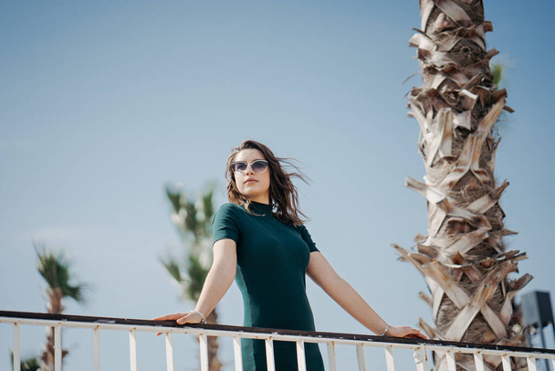 Krásná mladá brunetka kráčí po městě ve slunečních brýlích a pózuje na kameru. Slunečné počasí a promenáda v Antalyi - Fotografie, Obrázek