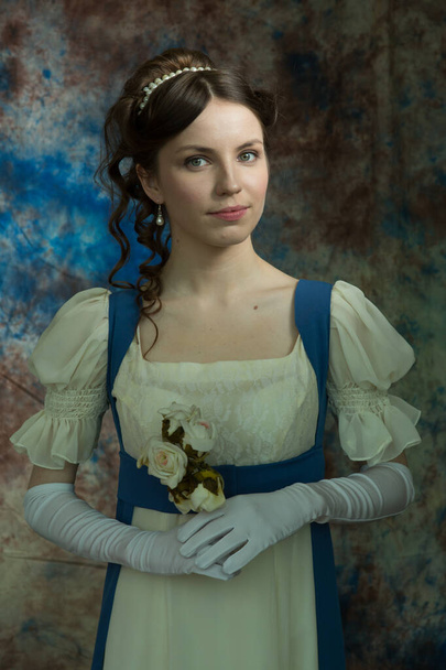 A young girl in a long dress of white and blue color. Looks directly at the camera. Holding white flowers. A woman in a retro dress. Historical reconstruction - Fotoğraf, Görsel