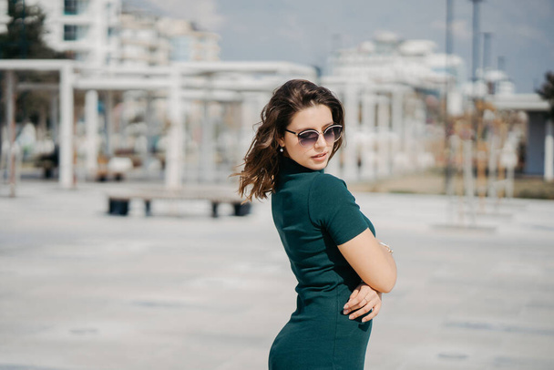 Güzel bir genç esmer kız şehirde güneş gözlükleriyle yürüyor ve kameraya poz veriyor. Antalya 'da güneşli hava ve gezinti güvertesi - Fotoğraf, Görsel