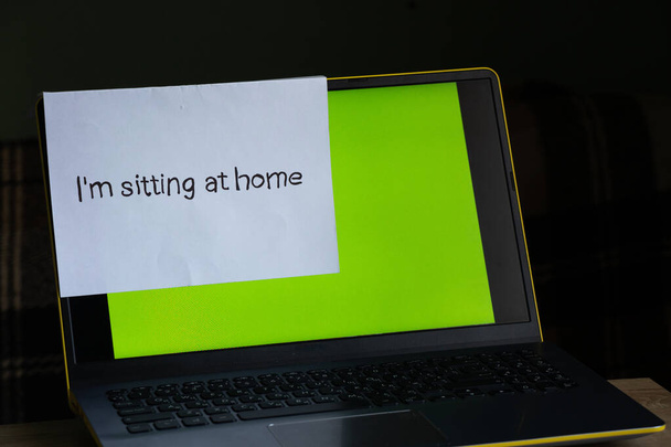 Laptop mit grünem Bildschirm auf einem Tisch in einem Zimmer zu Hause und ein Laken mit einer Inschrift in Englisch sitzt zu Hause in der Zeit. - Foto, Bild