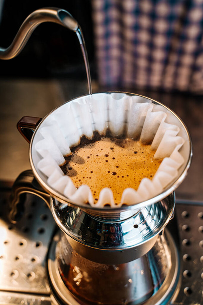 Método alternativo de elaboración de café. Primer plano del barman vertiendo agua de la tetera al filtro con café molido en el restaurante
. - Foto, imagen