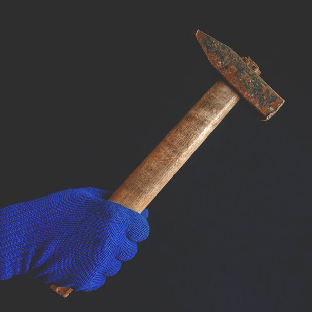Men's hand in blue glove with hammer in hand on a dark background - Photo, Image