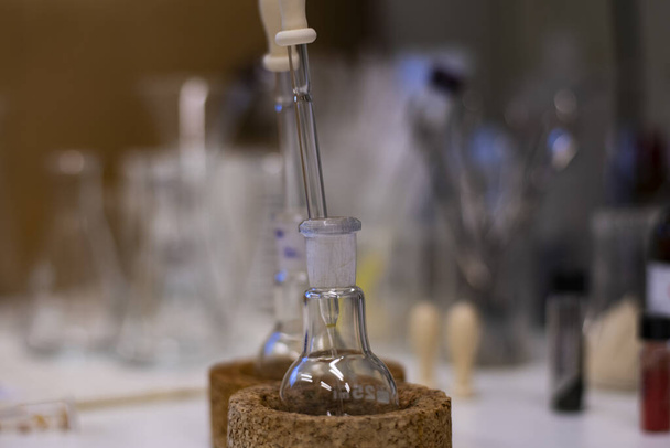 Pyöreäpohjainen pullo, jossa on lasinen kumitulppa kemiallisen synteesin edistämiseksi kemian laboratoriossa, jossa on kemikaaleja injektiopulloissa - Valokuva, kuva