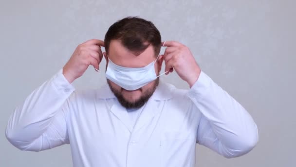 Il medico barbuto sta cercando di indossare una maschera protettiva sbagliata sulla testa. Scherzo. Concetto di igiene. prevenire la diffusione di germi e batteri ed evitare l'infezione con il virus della corona
 - Filmati, video