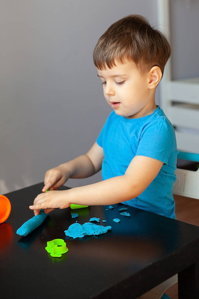 Odanda renkli kil kalıplarıyla oynayan çocuk evde küçük bir çocuk heykeli yapıyor. Anaokulu çocukları için eğitici oyunlar - Fotoğraf, Görsel