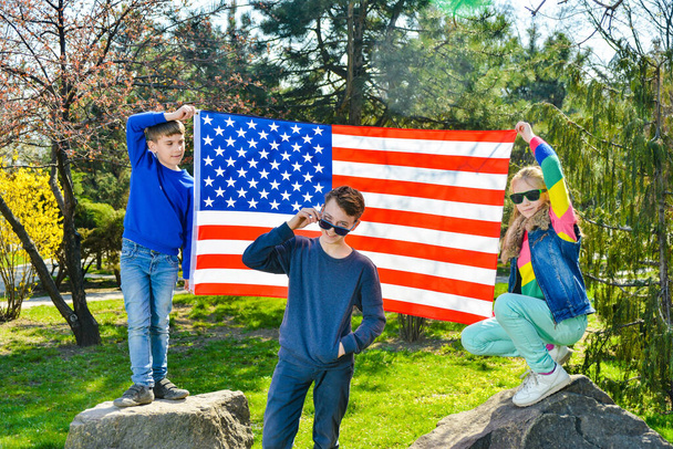 Teen guy in sunglasses with friends on the background of the American flag. - Zdjęcie, obraz