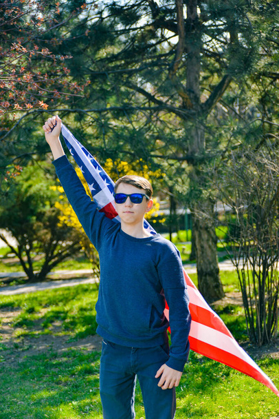 Un patriota adolescente alzò la mano con la bandiera americana verso l'alto come simbolo della vittoria e del patriottismo degli Stati Uniti
. - Foto, immagini
