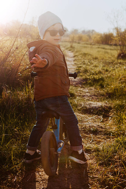A boy rides a balance bike in a clearing. Spring mood. Sun - Foto, Imagem