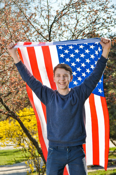 Ένας έφηβος πατριώτης κρατώντας την αμερικανική σημαία στην κορυφή πίσω από την πλάτη του ως σύμβολο της νίκης και του πατριωτισμού των ΗΠΑ. - Φωτογραφία, εικόνα