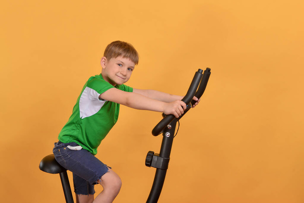 The boy goes in for sports on a stationary bike and does cardio training. - Фото, зображення