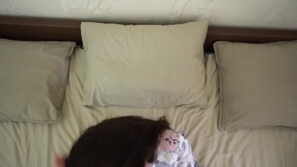 Single aantrekkelijke brunette meisje in bloemenblouse ligt op een beige kussen, zet op een beschermende medische masker, sluit haar ogen, slaapt in bed bovenaanzicht. Beschermingsperiode van covid-19 virusdreiging.  - Video