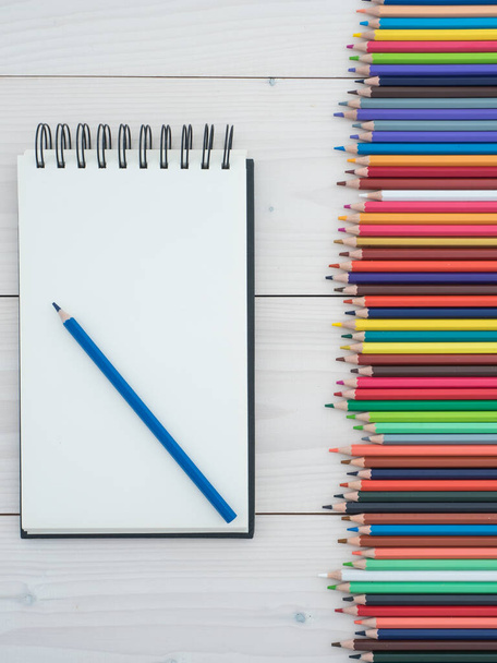 Set of colored pencils arranged in a row and notebook on wooden background. top view - Foto, Imagen