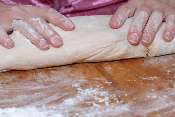 Female hands knead the dough on a wooden table. The process of preparing fresh elastic baking dough. Table and hands in flour. Natural home cooking. - Photo, Image