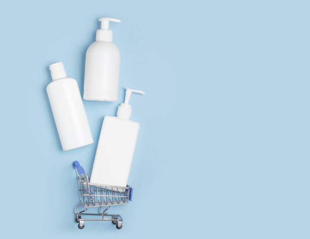 White cosmetic jars with shampoo, shower gel, hand soap lie in shopping carts on a blue background. Online store for home - Fotografie, Obrázek