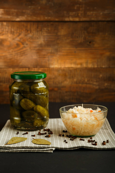Jars with pickled cucumbers and sauerkraut on a wooden table on a black background. - Foto, imagen