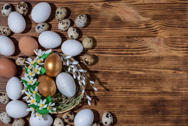 Easter eggs in basket filled with straw and yellow flowers and willow on wooden rustic vintage background. Preparation for holiday. Easter decorations - Photo, Image