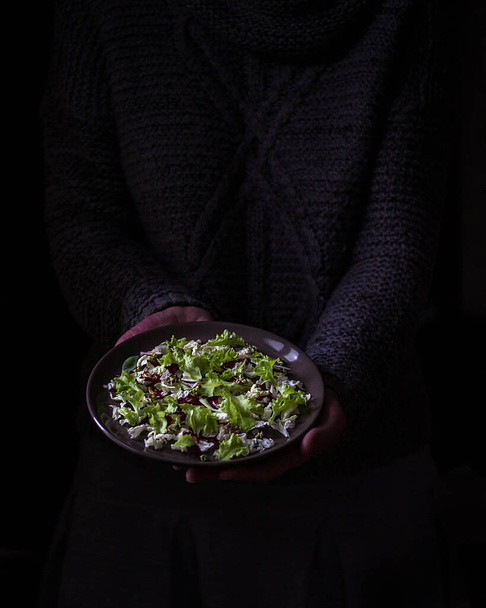Zielona sałatka na talerzu w dłoniach na ciemnym tle, minimalizm. - Zdjęcie, obraz