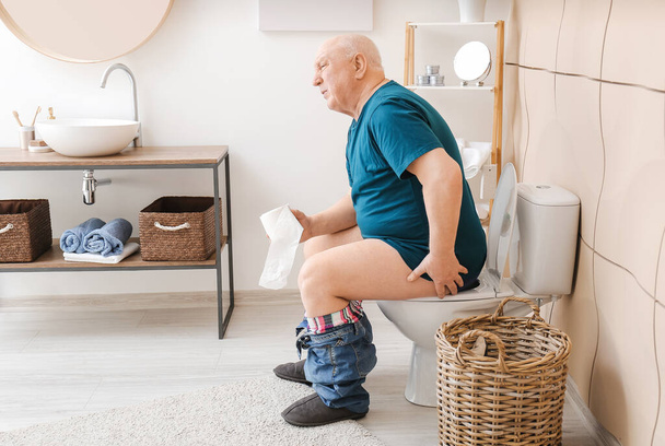 Idős férfi aranyér ül WC-csészében a mosdóban - Fotó, kép