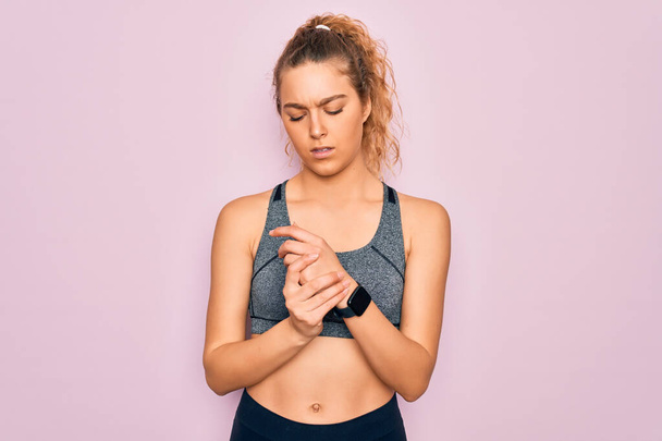 Young beautiful blonde sportswoman with blue eyes doing exercise wearing sportswear Suffering pain on hands and fingers, arthritis inflammation - Фото, изображение