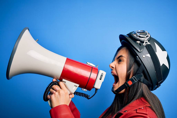 Mujer hispana con casco de moto vintage gritando enojada en protesta a través del megáfono. Gritando emocionado en ludspeaker hablando y gritando noticias - Foto, imagen