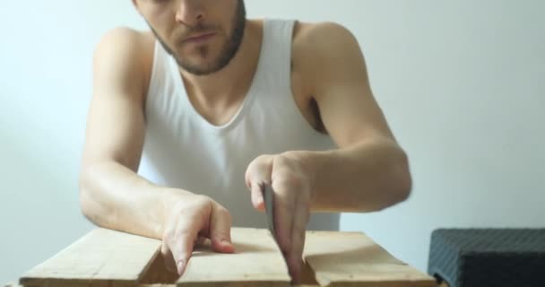 Ele fica em casa, jovem homem branco lixando uma caixa de madeira em um fundo branco
  - Filmagem, Vídeo